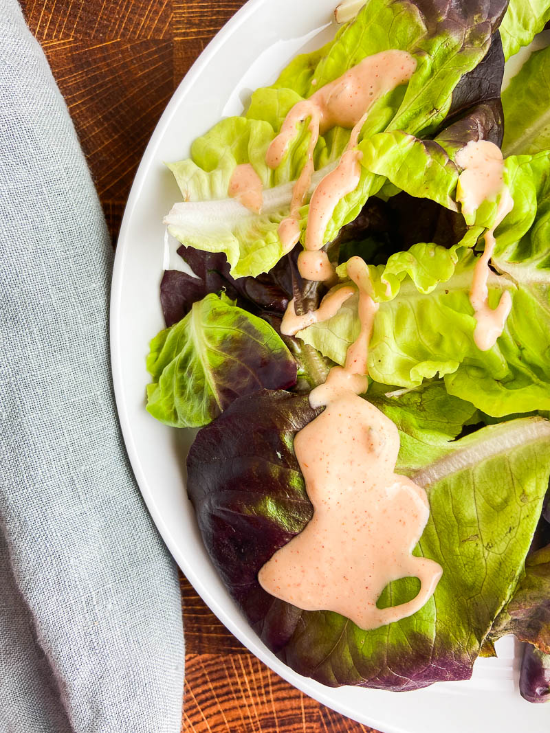 Thousand Island Dressing on a green salad on a white plate. 