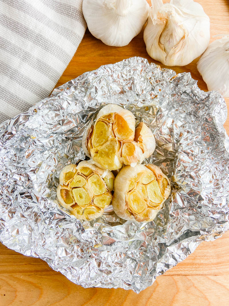 Overhead photo oven roasted garlic on aluminum foil.