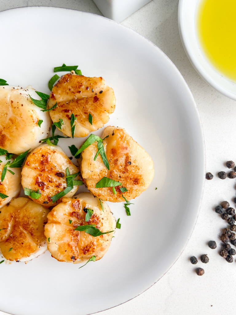 Overhead photo of seared sea scallops on white plate. 