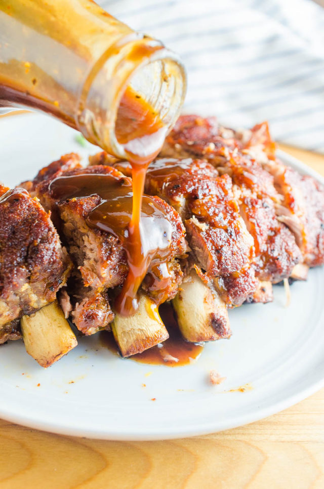 Pouring BBQ sauce on ribs on a white plate. 