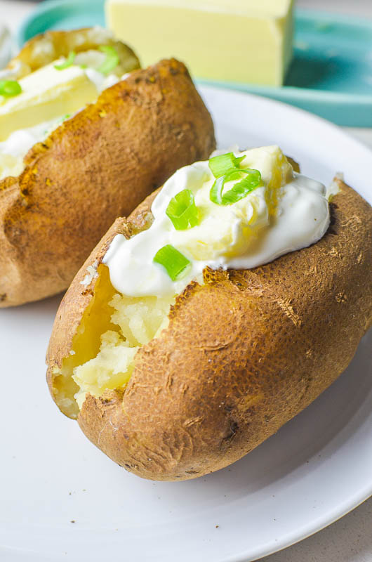 Instant pot potatoes on a white plate. Topped with butter sour cream and green onions. 