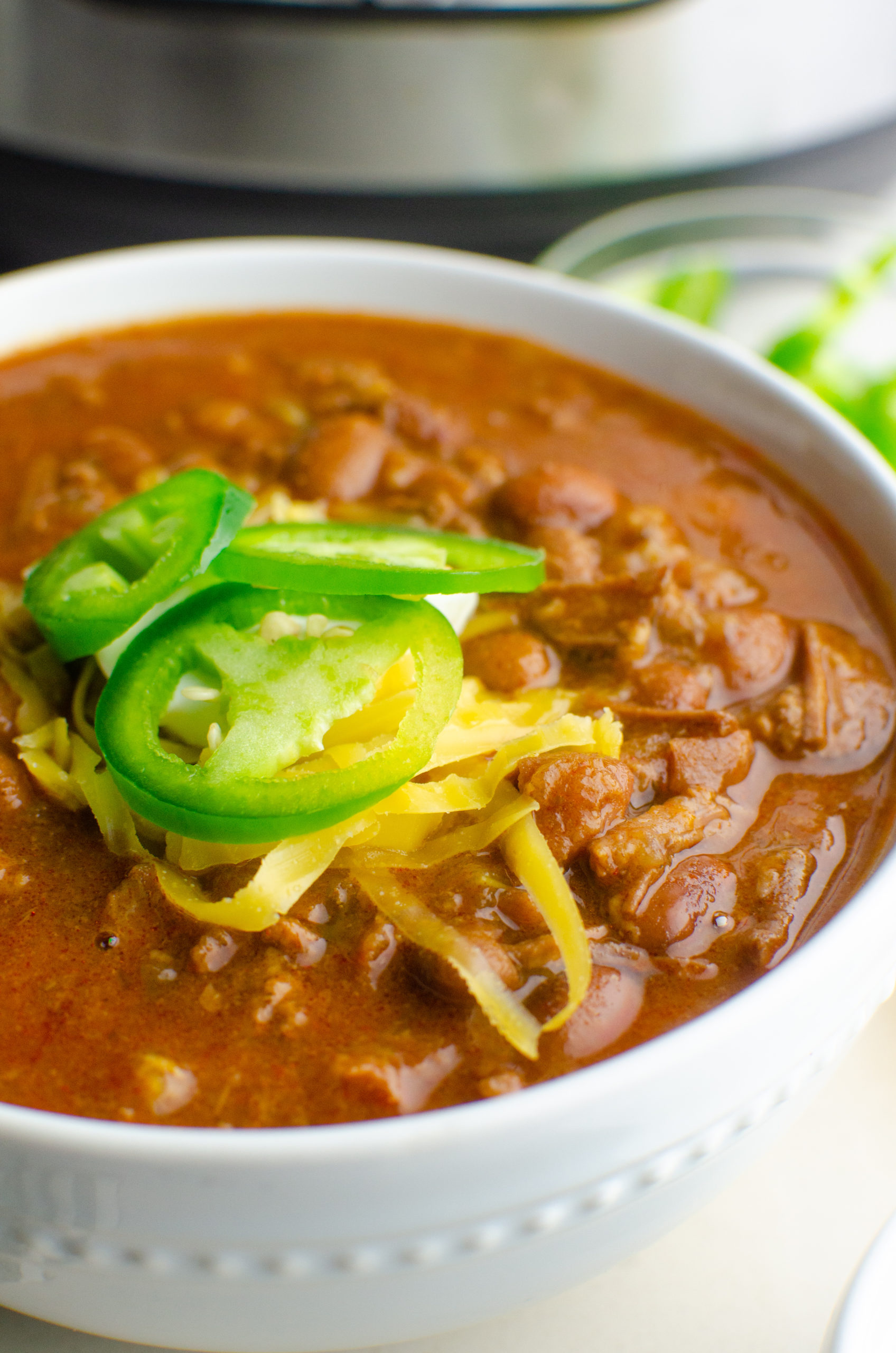 Side angle photo of instant pot chili topped with cheese and jalapenos. 