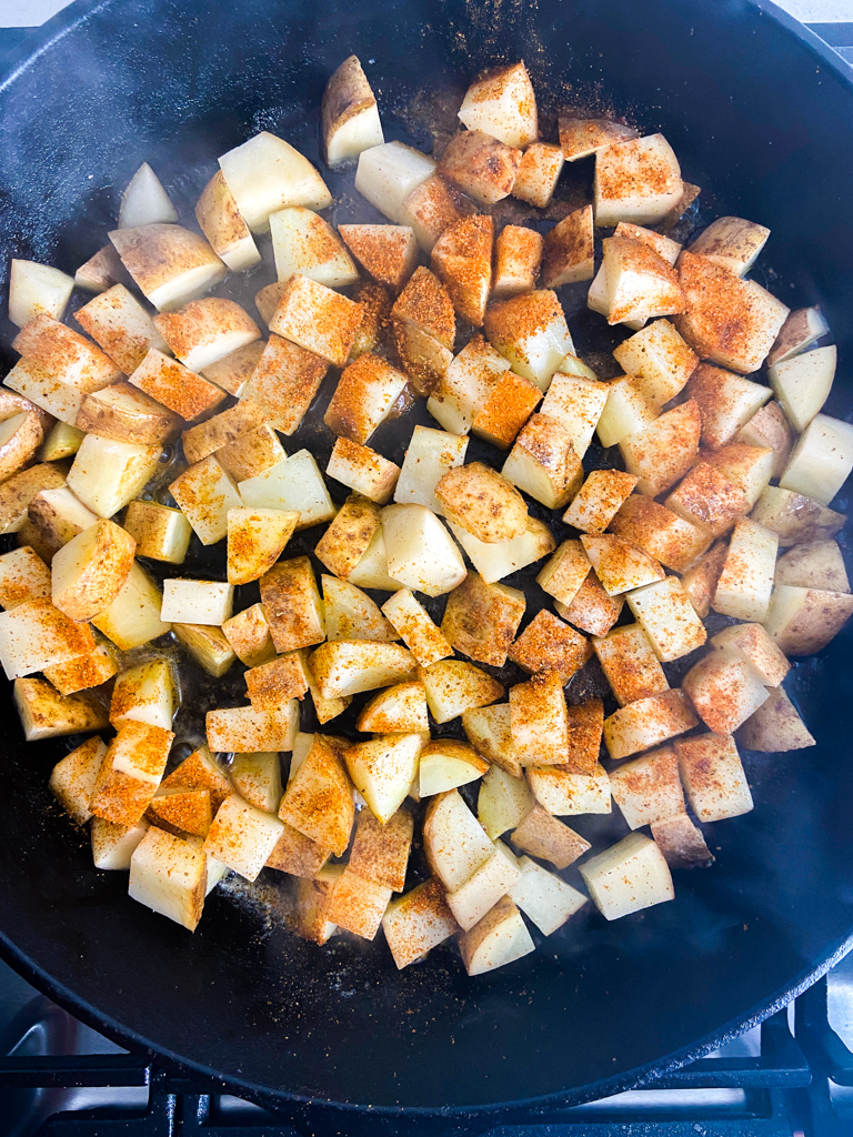 Frying potatoes in a cast iron skillet with Old Bay Seasoning sprinkled on top. 