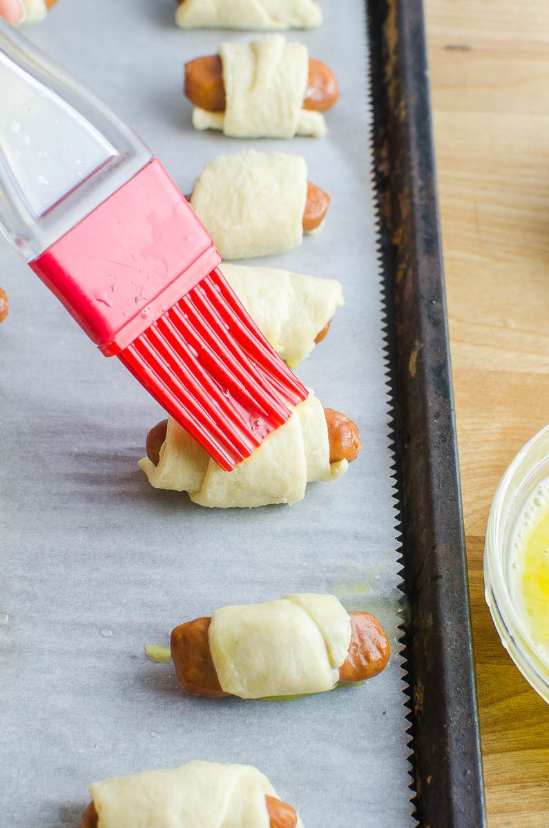 Using a brush to brush egg onto mini pigs in a blanket. 