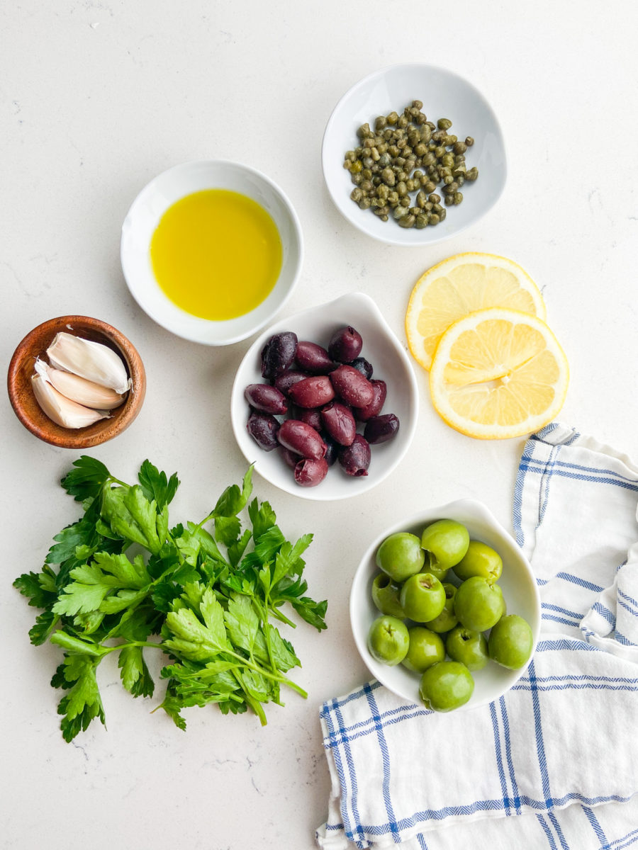 Olive tapenade ingredients on white marble background. 