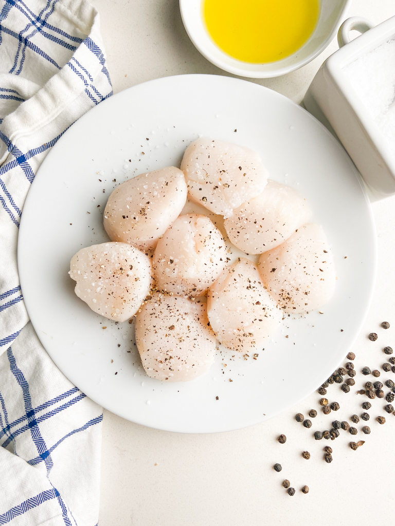 Overhead photo of scallops seasoned with salt and pepper. 