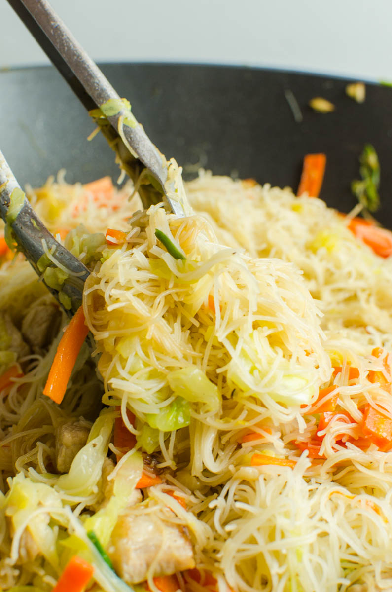 Tongs picking up pancit noodles and vegetables. 