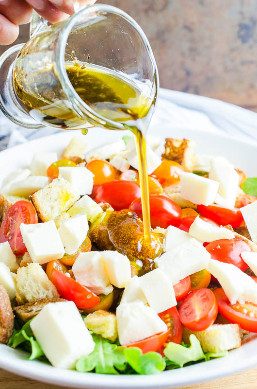 Pouring balsamic vinaigrette on panzanella salad.