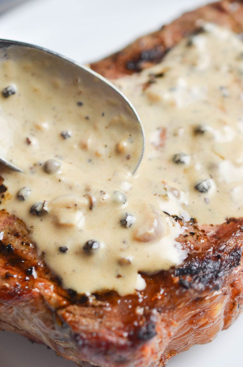 Spooning peppercorn sauce on steak.