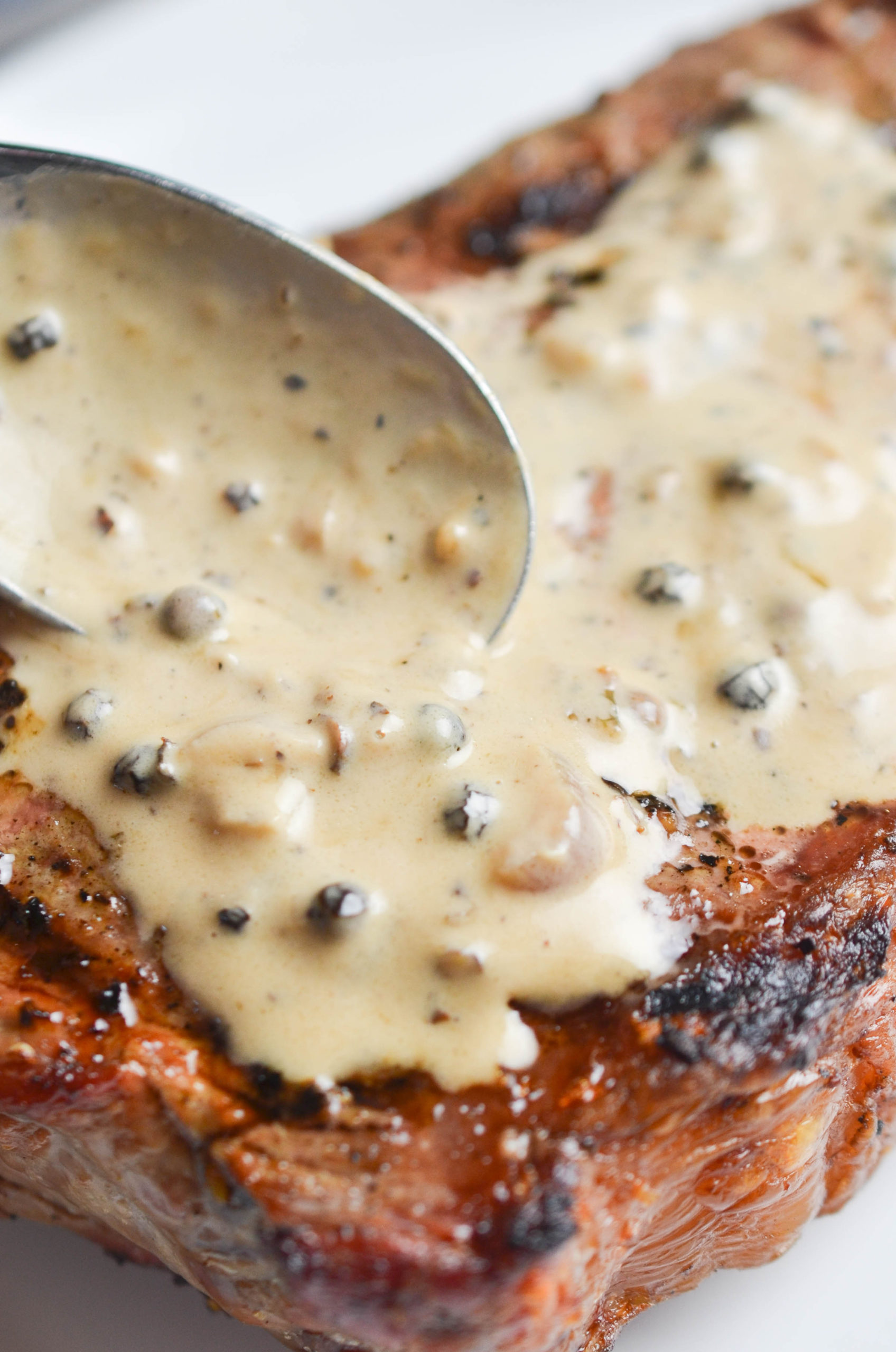 Spooning peppercorn sauce on steak. 