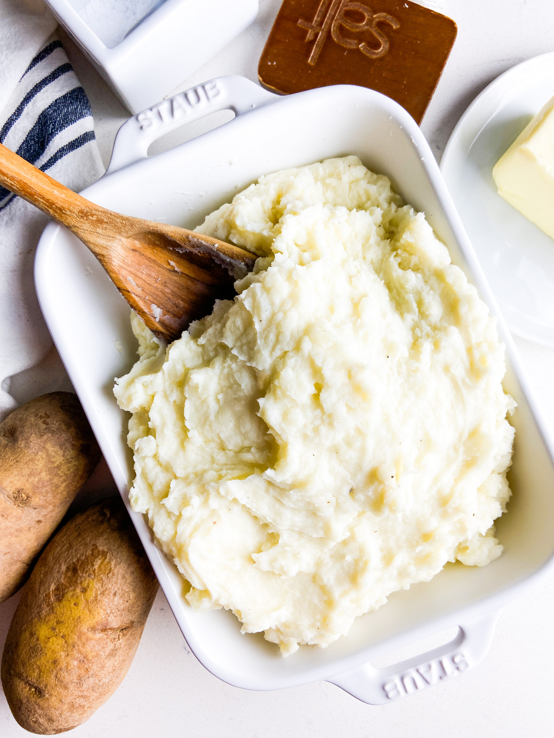 Overhead photo of mashed potatoes in a white dish with wooden spoon. 