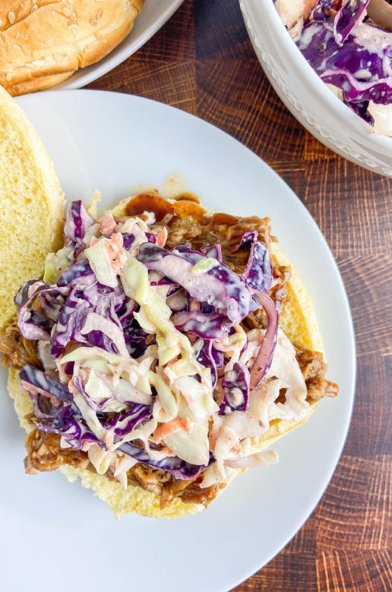 Overhead photo of BBQ pulled pork sandwich on a white plate on a wooden background.