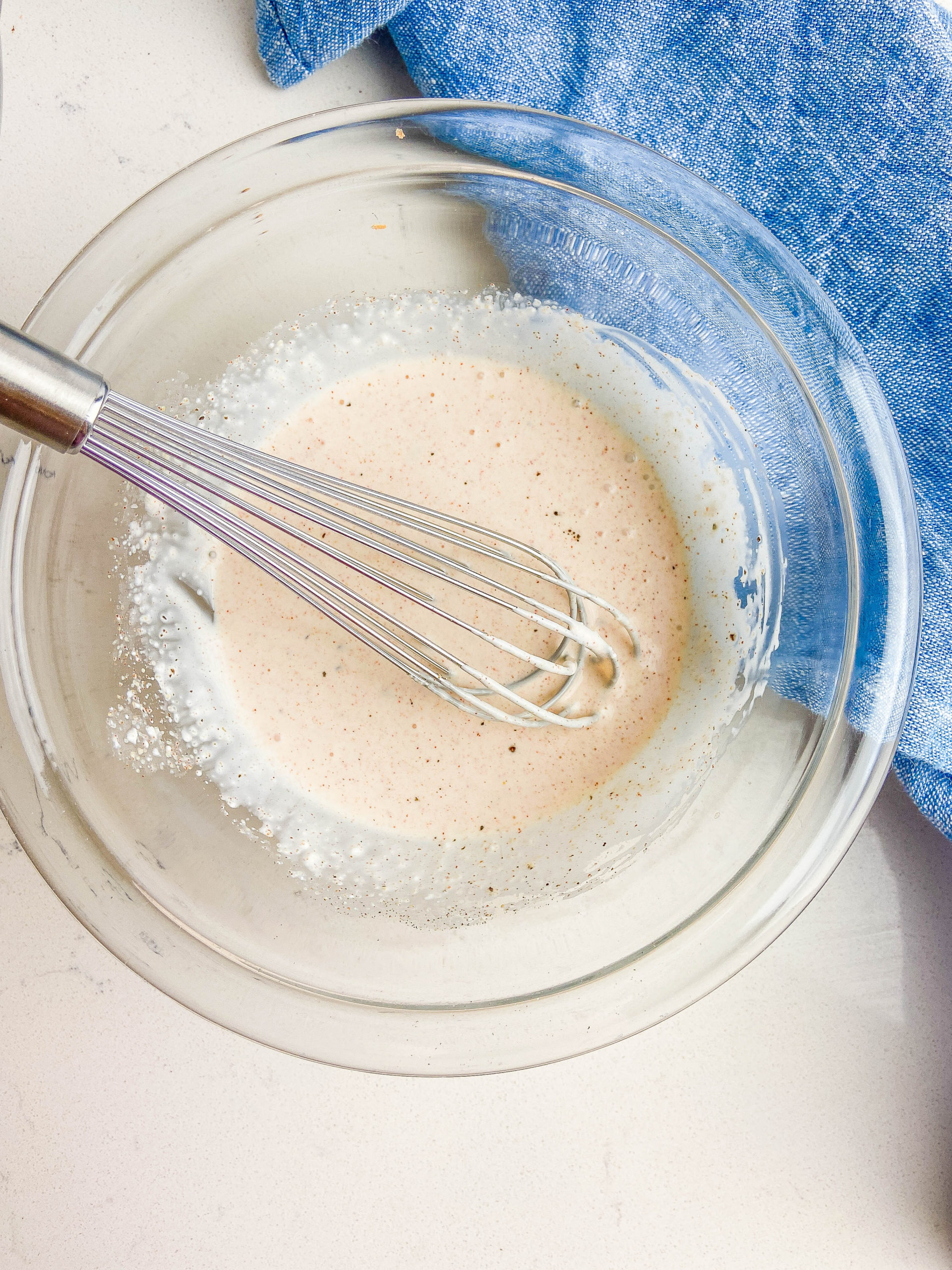 Whisking dressing ingredients together in a clear glass bowl. 