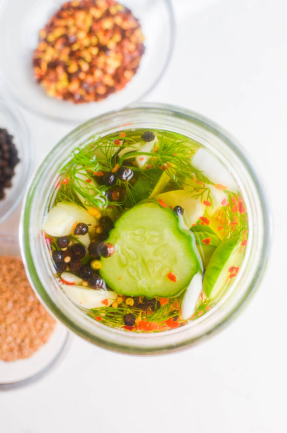 Overhead photo of pickles with crushed red peppers, mustard seeds and peppercorns off to the side.