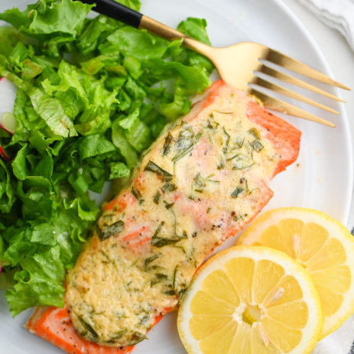 Overhead photo of salmon with dijon tarragon sauce on white plate with salad and lemon slices.