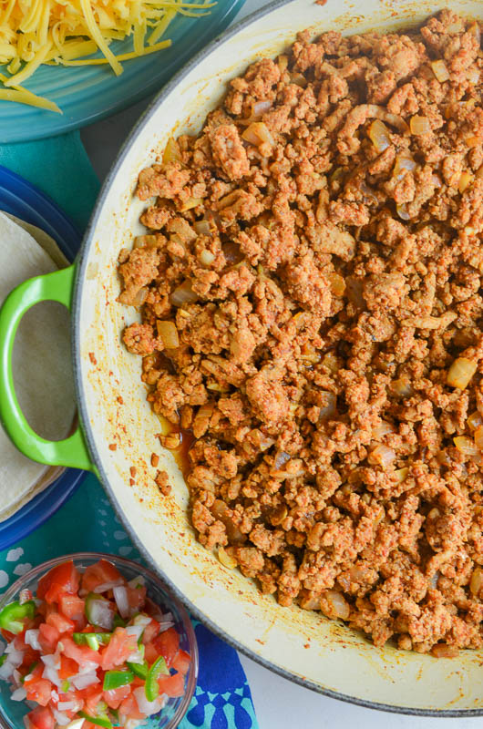 Seasoned taco meat in a pan with pico de gallo, and shredded cheese on a plate