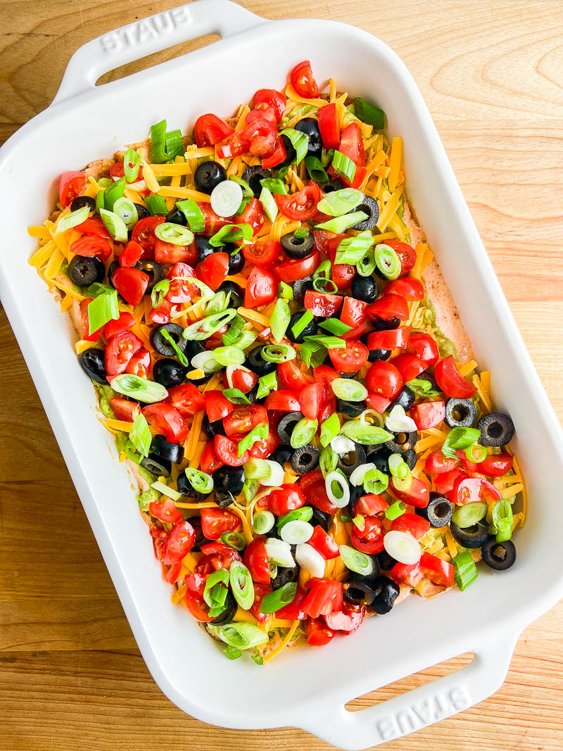 Seven Layer Taco Dip in a white dish on wooden cutting board. 