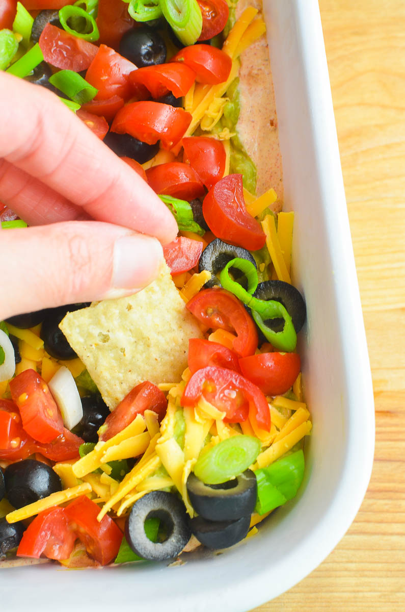 Dipping a chip into taco dip in a white dish. 