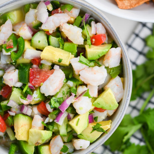 Overhead photo of shrimp ceviche in a bowl with a lime, tortilla chips and cilantro in the background.