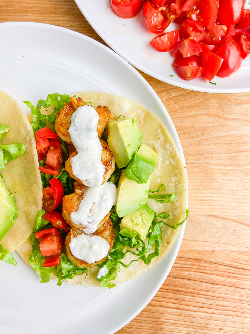 Overhead photo of shrimp tacos with cilantro cream sauce on white plate.