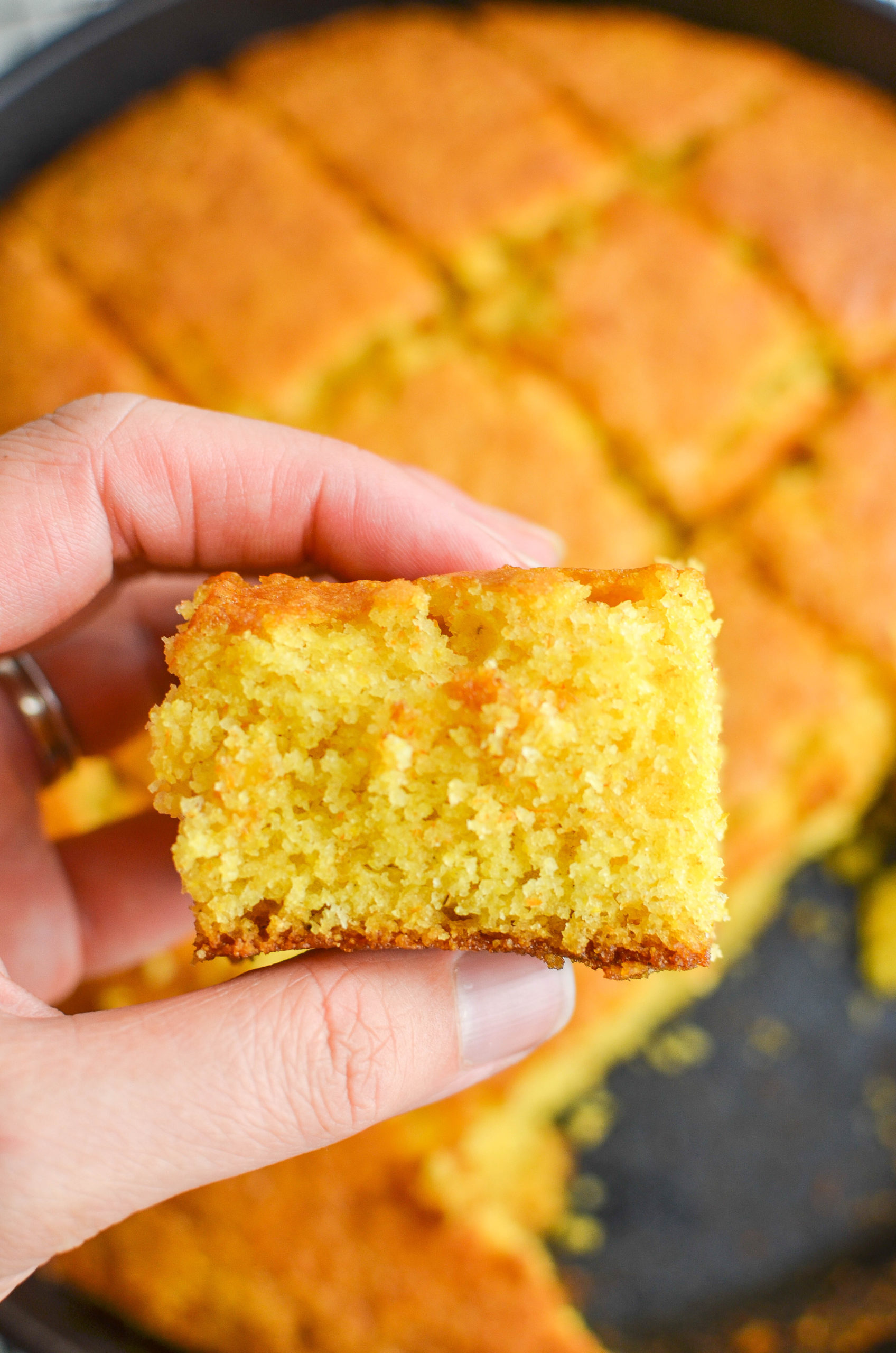 Hand holding a square of cornbread. 