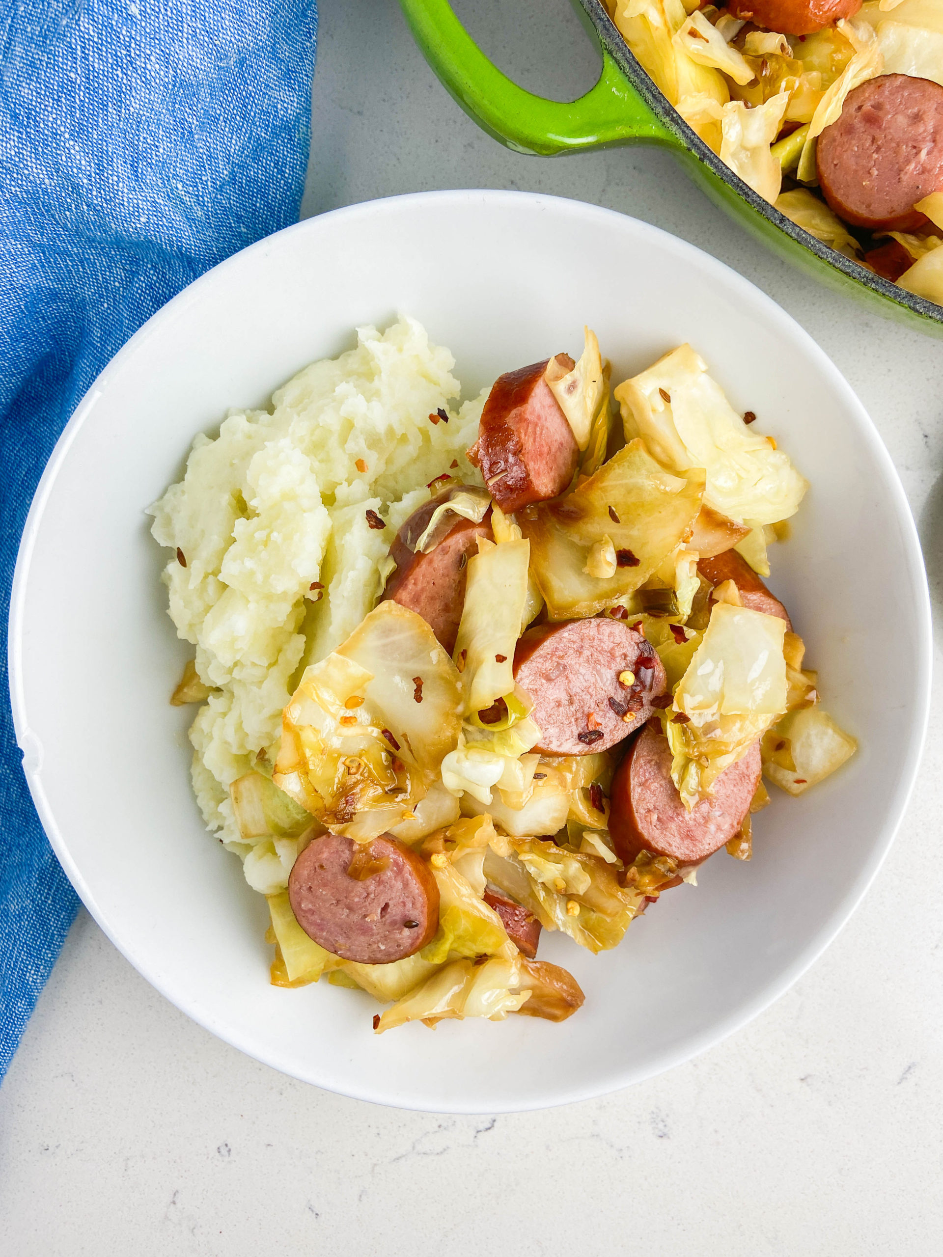Kielbasa and cabbage with mashed potatoes in a white bowl. 