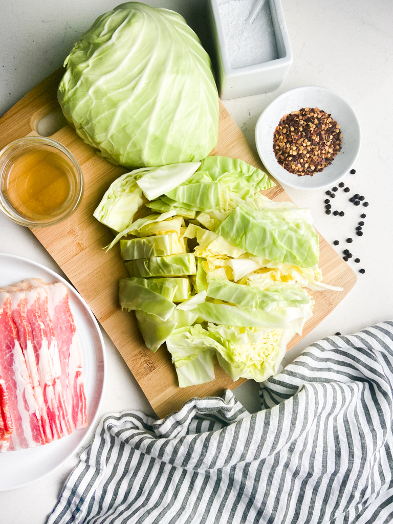 Overhead photo of ingredients for southern fried cabbage with bacon on a wooden cutting board. 