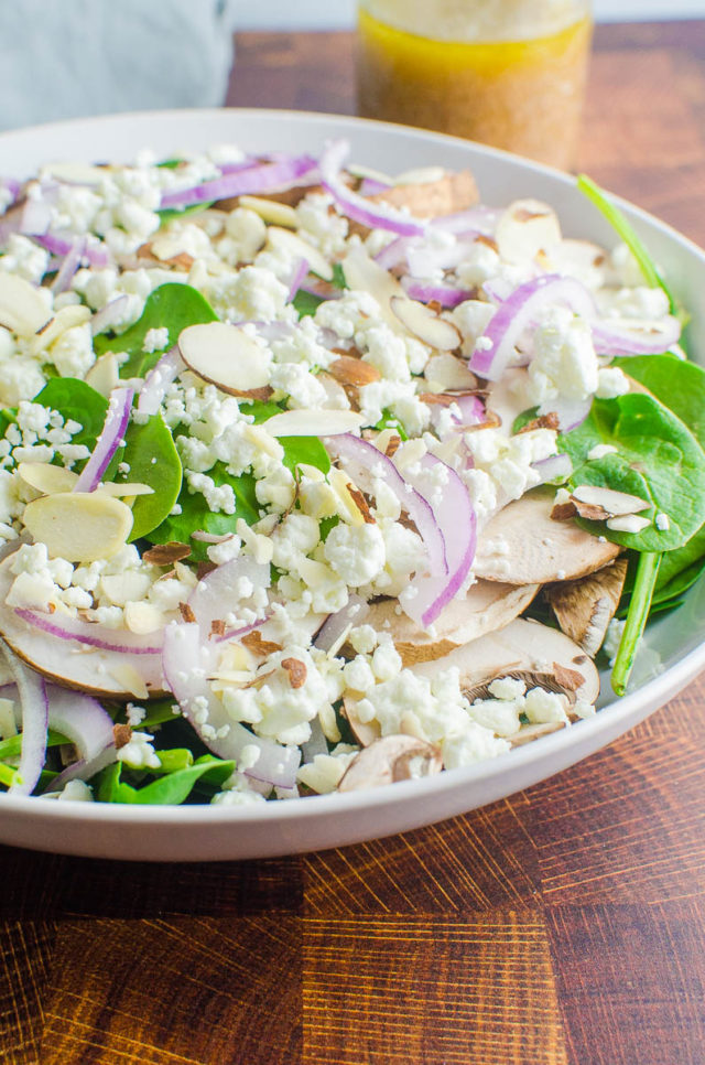 Side angle photo of spinach salad with goat cheese, mushrooms and red onions