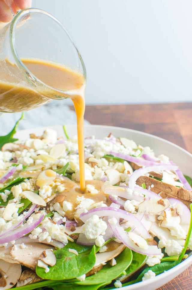 Pouring spinach salad dressing onto salad. 