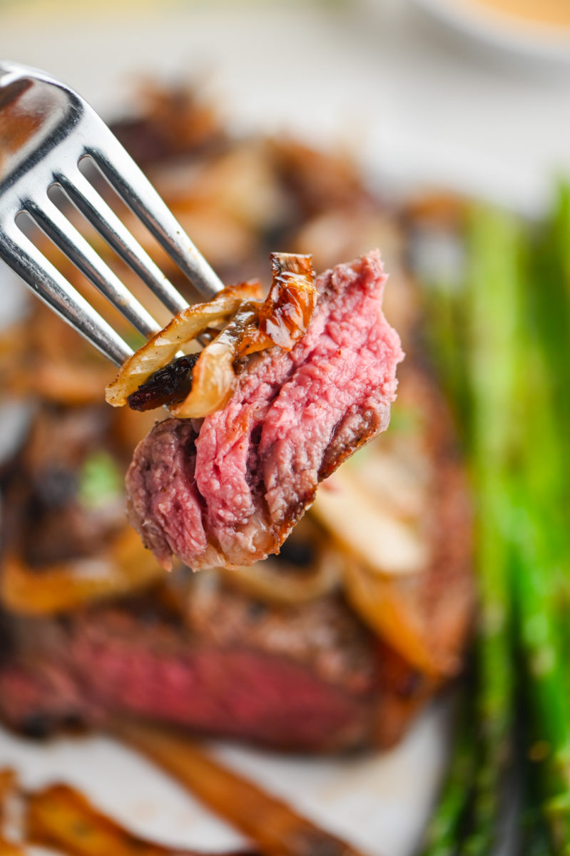 Slice of steak with onions on a fork. 