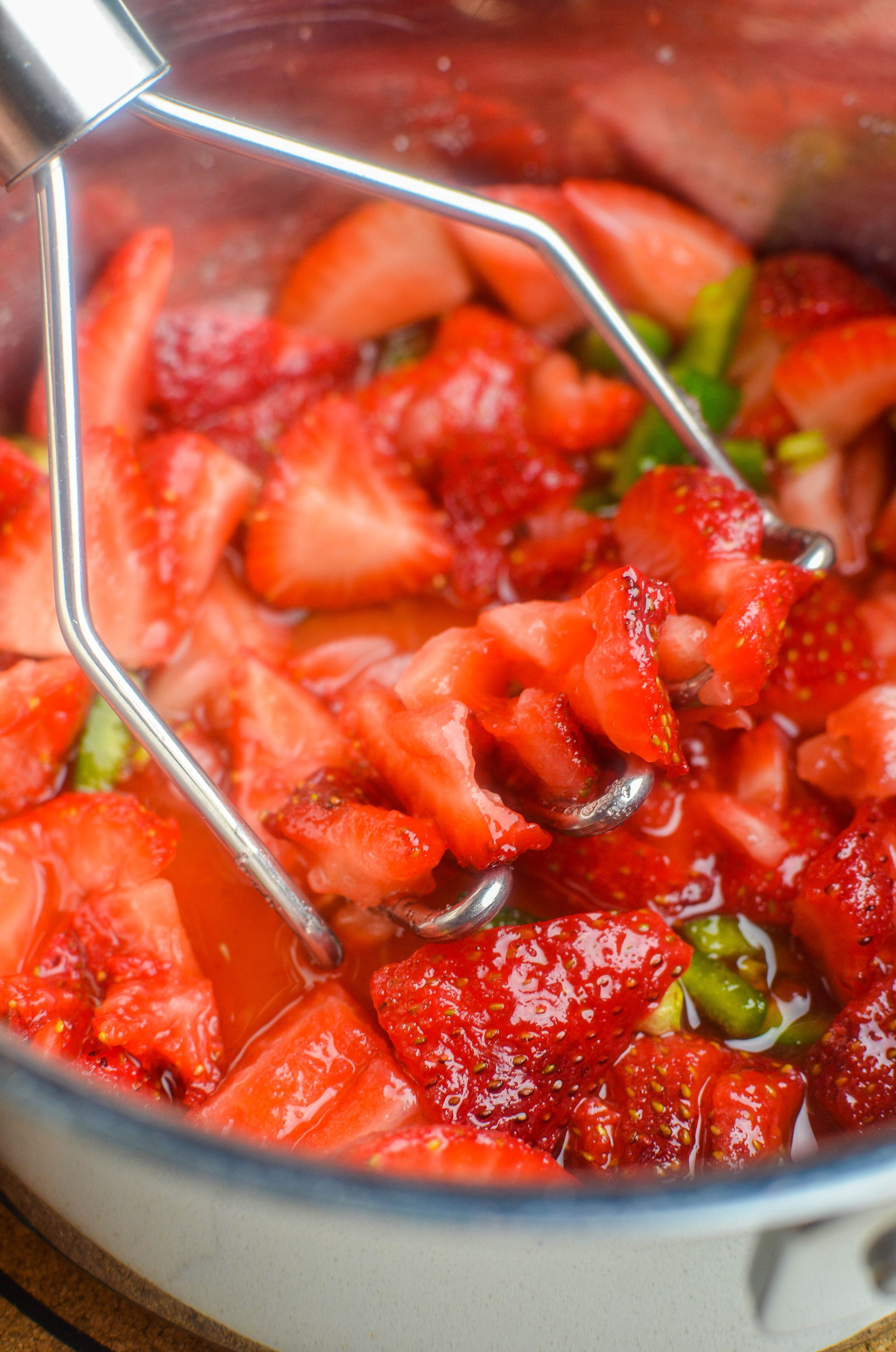 mashing ingredients for jam in a saucepan using a potato masher. 