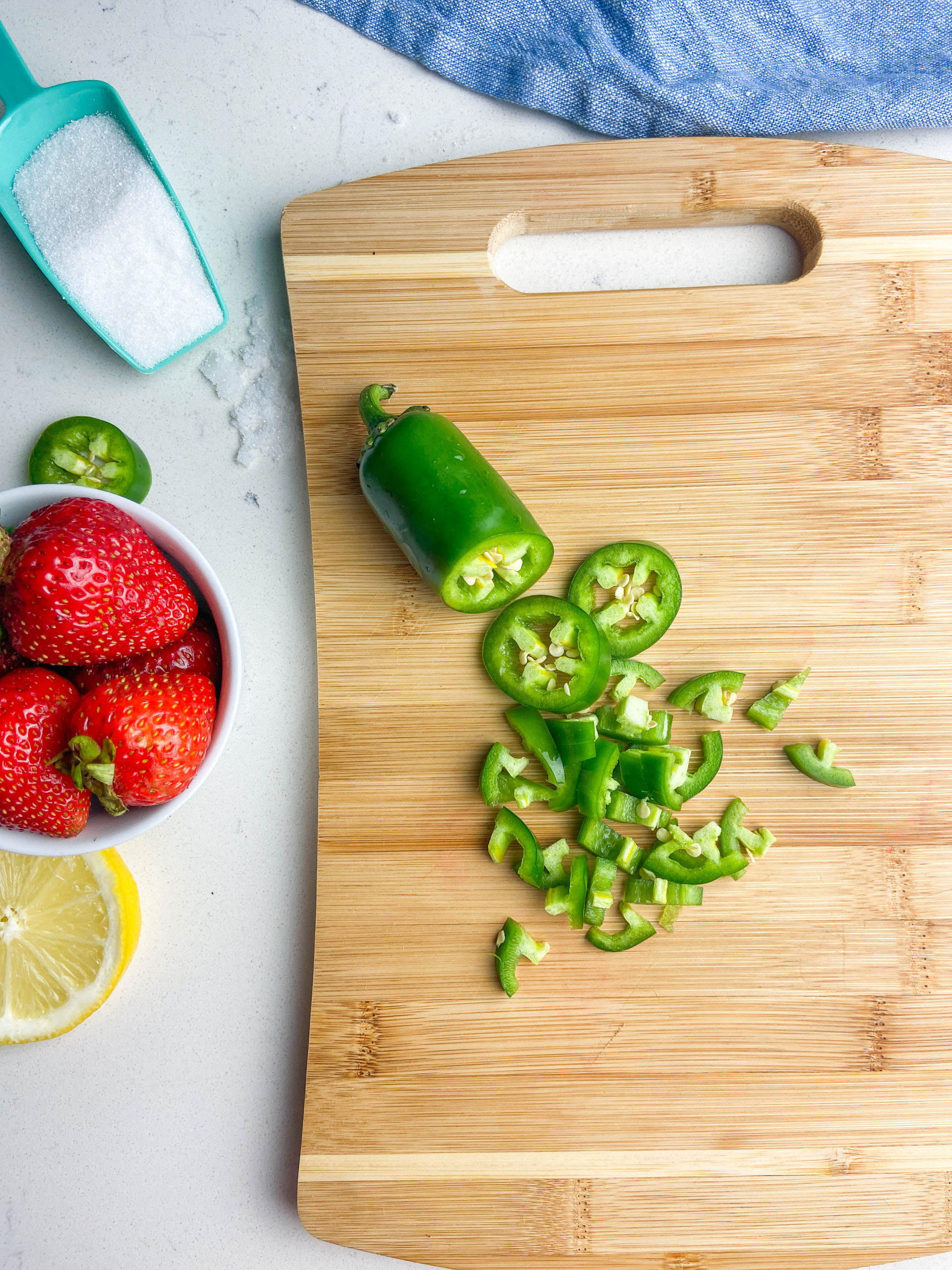 Jalapenos sliced on a wooden cutting board with strawberries, sugar and lemon slices. 