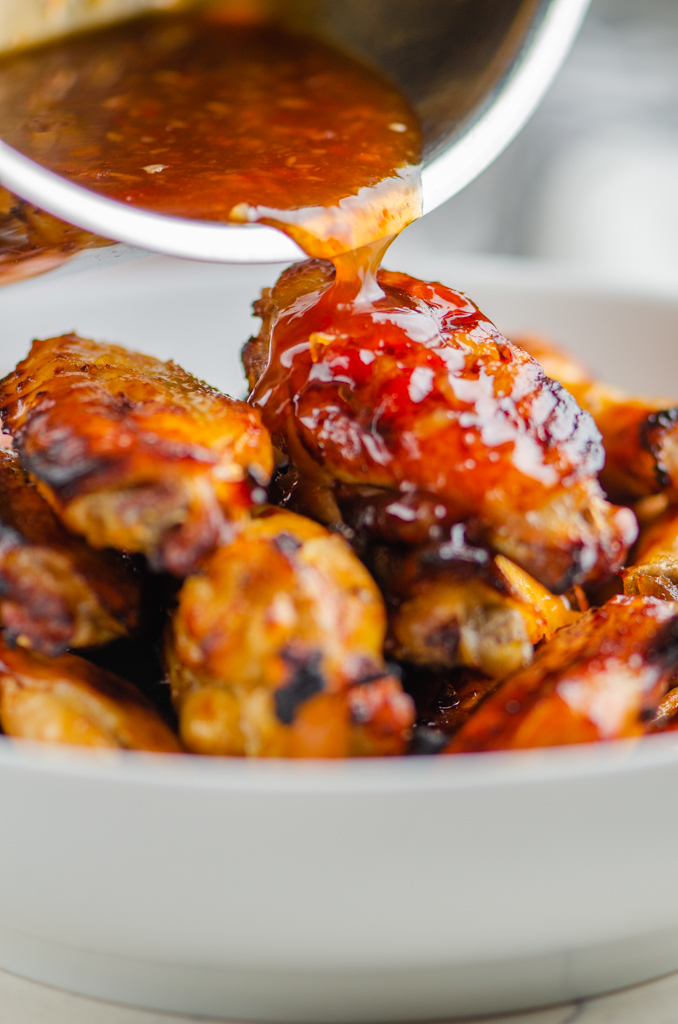 Pouring sweet chili sauce over baked chicken wings. 