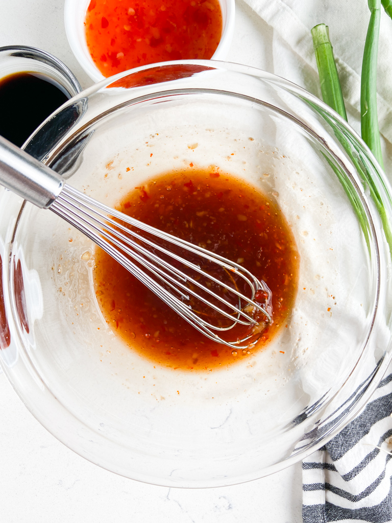Ingredients for sweet chili sauce in a glass bowl with a whisk.