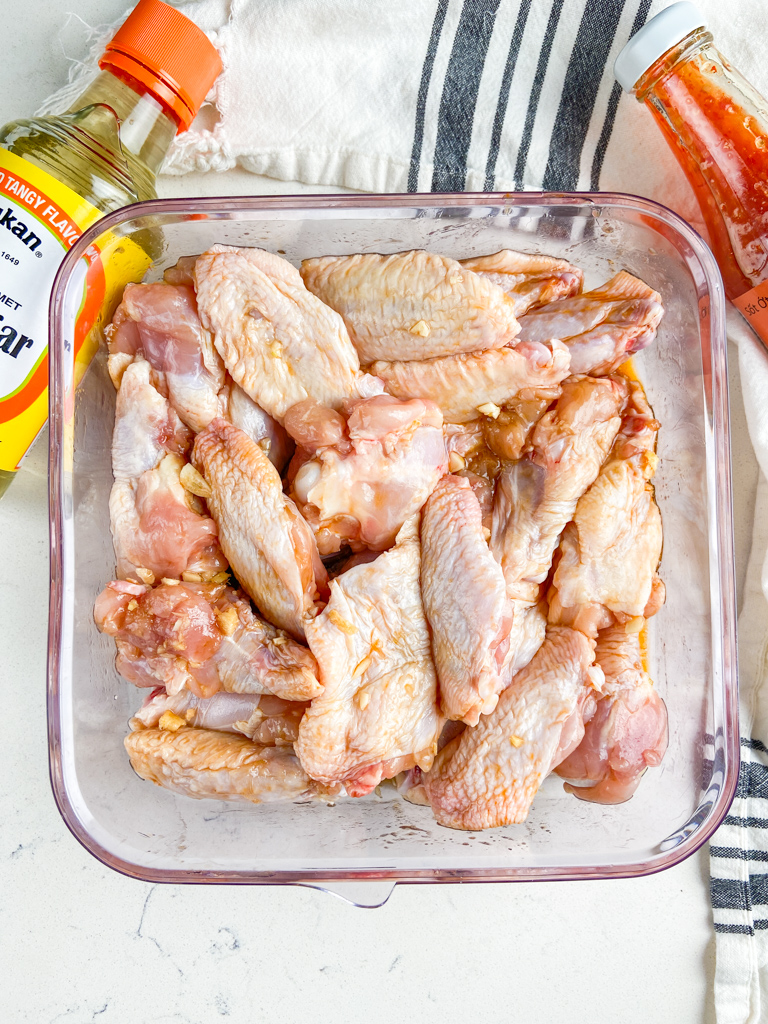Chicken wings marinating in a clear plastic container.