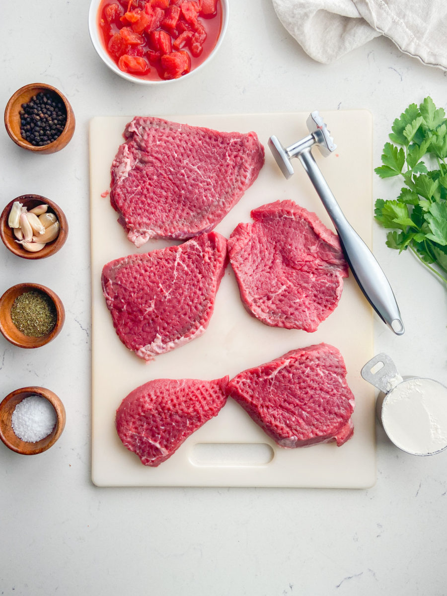 Round steak that has been tenderized with a meat mallet on white cutting board.