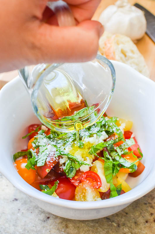 Pouring olive oil onto tomato bruschetta topping in a white bowl. 