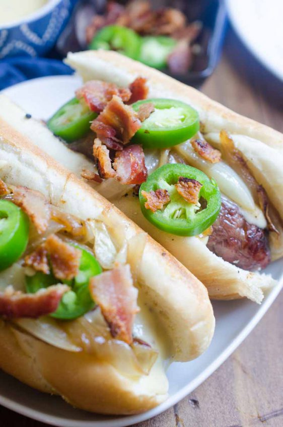 Ultimate cheesy brats are loaded with caramelized onions, cheese sauce, jalapeños and bacon. They are the perfect way to celebrate National Bratwurst day!