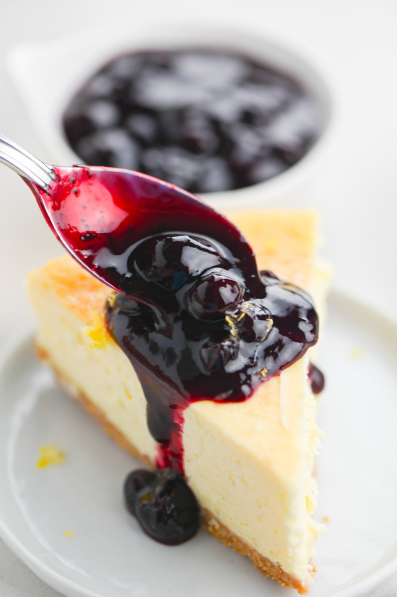 Spooning blueberry sauce over vanilla bean cheesecake. 