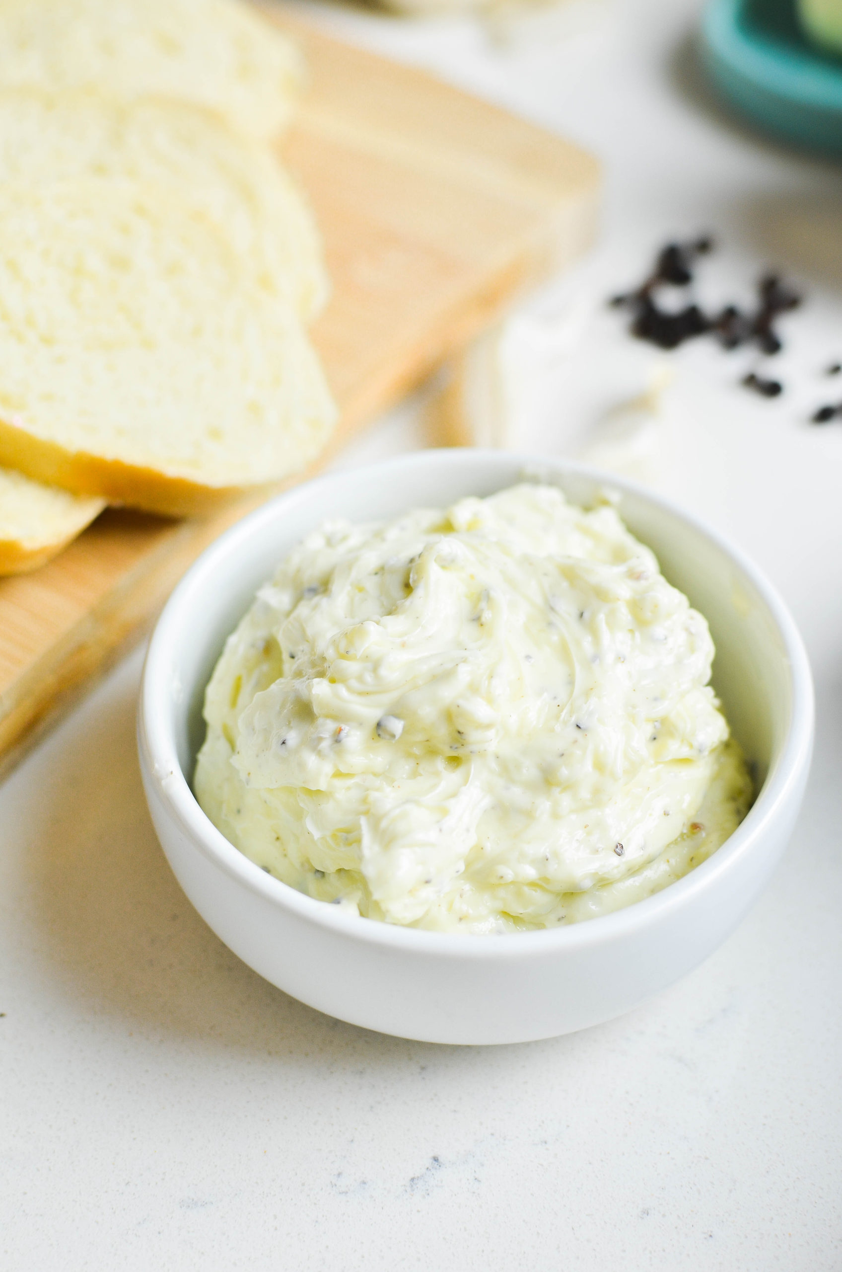 Whipped butter with garlic and black pepper in a white bowl. Bread and peppercorns in the background. 