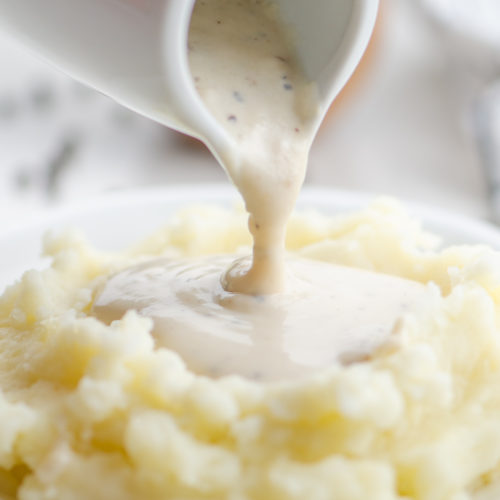 Pouring white country gravy on mashed potatoes.