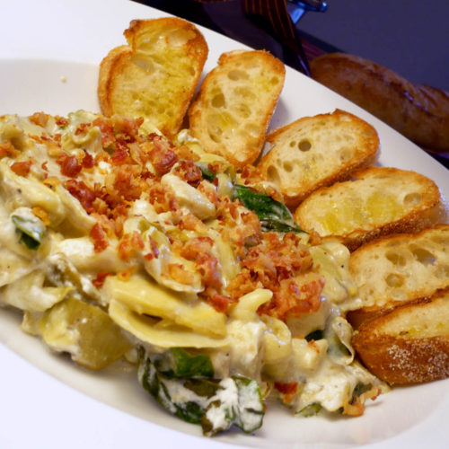 Artichoke and spinach dip in a bowl with toasted crostini.