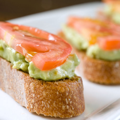 Avocado and tomato crostini on white plate.