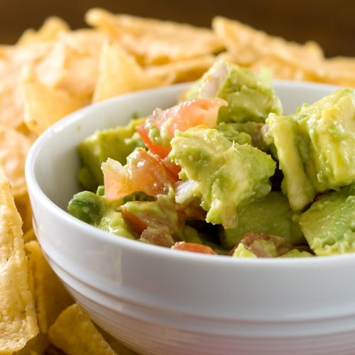 Avocado salsa in white bowl with tortilla chips.