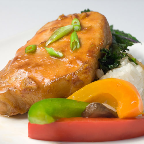 Glazed asian style pork chops on plate with bell peppers.