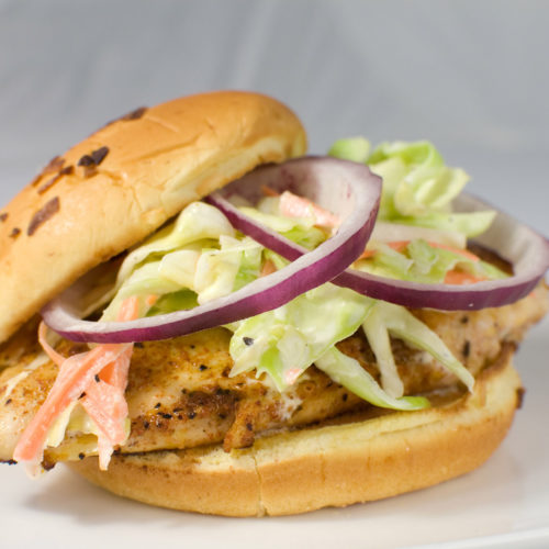 Cajun chicken sandwich topped with slaw and red onion.