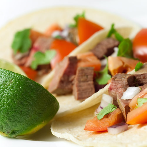 3 carne asada tacos on plate with lime.