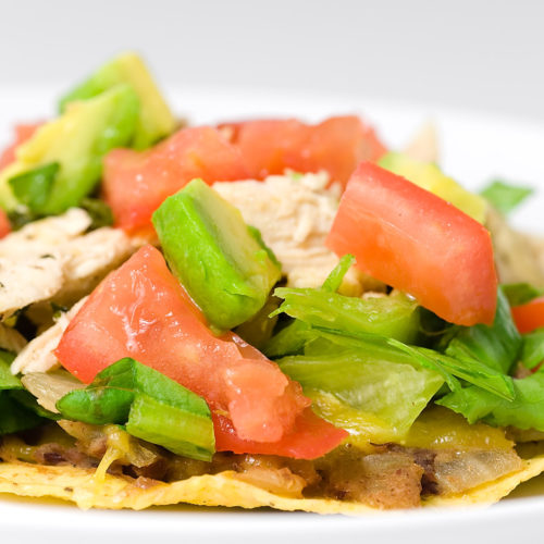 chicken tostada topped with avocado and diced tomato.