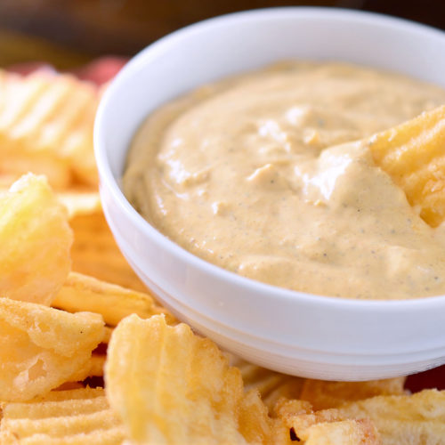 Creamy pumpkin sage dip in white bowl with chips