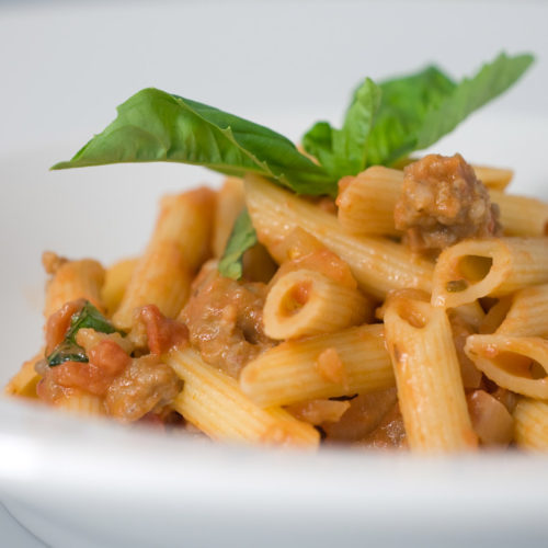 Creamy tomato penne in white bowl.